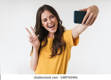 Image of beautiful brunette woman laughing and showing peace sign while taking selfie photo on cellphone isolated over white background - Shutterstock ID 1489765496