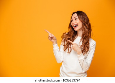 Image of beautiful cute young woman standing isolated over yellow background pointing. Looking aside.