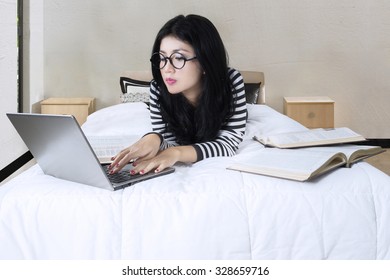 Image Of Beautiful Female College Student Using Laptop Computer And Reading Books On The Bed