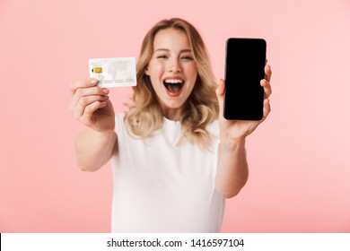 Image Of A Beautiful Happy Young Blonde Woman Posing Isolated Over Pink Wall Background Holding Credit Card Using Mobile Phone Showing Display.