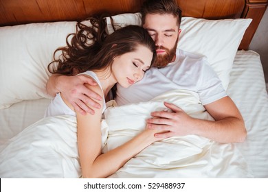 Image of beautiful happy young couple sleeping in bed while hugging