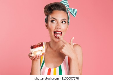 Image of beautiful pin up woman isolated over pink wall background holding cake.