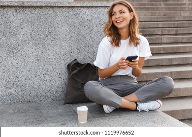 Image of beautiful stylish woman sitting on street stairs with legs crossed on summer day and holding mobile phone - Shutterstock ID 1119976652