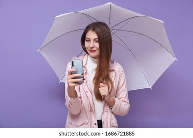 Image Of Beautiful Tender Attractive Young Woman Making Selfie, Talking Over Videocall, Holding Smartphone And Umbrella, Having Long Hair, Bad Weather, Raining. People And Technology Concept.