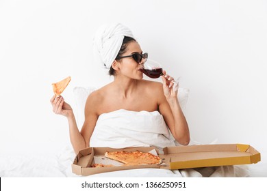 Image Of A Beautiful Woman With Towel On Head Lies In Bed Under Blanket Isolated Over White Wall Background Wearing Sunglasses Eat Pizza Drinking Wine.