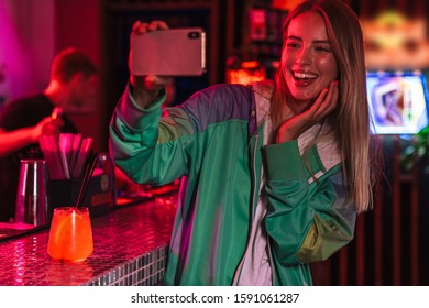 Image of beautiful young caucasian woman taking selfie photo on smartphone in bar over neon lightening - Powered by Shutterstock