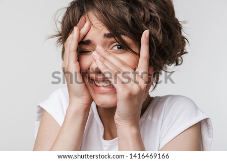 Image of a beautiful young pretty scared woman posing isolated over white wall background covering face.