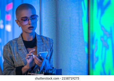 Image Of A Beautiful Young Woman Posing Against A Led Panel. Shaved Head Teenager With Alternative Look Making Urban Portraits