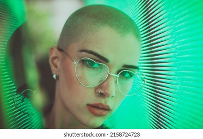 Image Of A Beautiful Young Woman Posing Against A Led Panel. Shaved Head Teenager With Alternative Look Making Urban Portraits