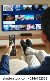 imagen de detrás de un hombre irreconocible sentado en el sofá con las piernas estiradas buscando contenido para ver en televisión