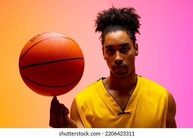 Image of biracial basketball player spinning basketball on pink to orange background. Sports and competition concept. - Powered by Shutterstock