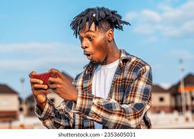 image of a black African youth on dreadlocks playing game on smartphone, man connected to wireless connection and wireless technology - Powered by Shutterstock