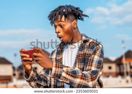 image of a black African youth on dreadlocks playing game on smartphone, man connected to wireless connection and wireless technology