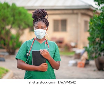 image of black nurse with face mask-young African health worker holding tablet with her stethoscope around the neck-portrait of beautiful African student nurse in her scrub dress during the covid-19 