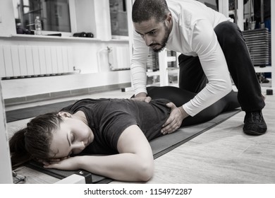 Image With Black And White Filter Of Physical Therapist Helping Adult Female With Ab Exercise And Weighlifting Machine In Background