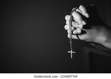 Image black and white woman hand holding rosary against cross and praying to God at church.