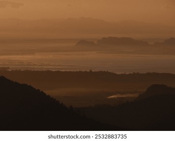 The image is a blurry photo of a mountain range with a hazy sky. The mountains are covered in trees and the sky is a mix of orange and pink hues - Powered by Shutterstock