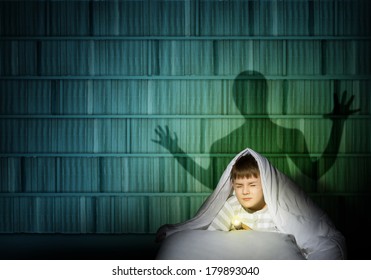 image of a boy under the covers with a flashlight the night afraid of ghosts