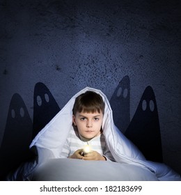 image of a boy under the covers with a flashlight the night afraid of ghosts