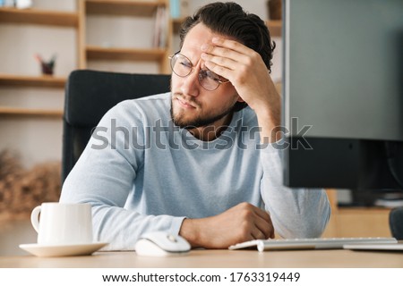 Image of brooding bearded programmer man wearing eyeglasses working with computer in office