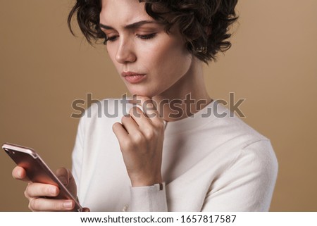 Image of brooding seductive woman using cellphone and thinking isolated over beige background