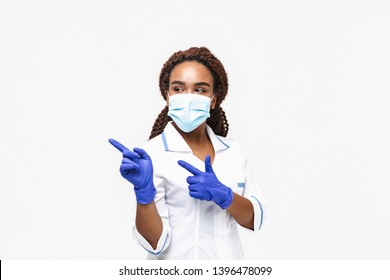 Image Of Brunette African American Nurse Or Doctor Woman Wearing Medical Face Mask And Disposable Gloves Pointing Fingers At Copyspace Isolated Against White Background