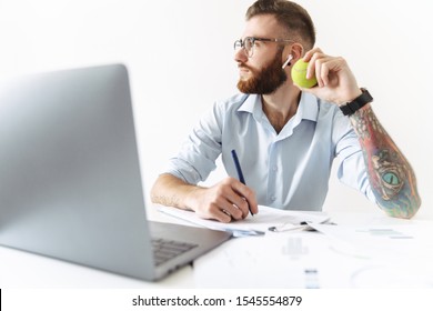 Image of brunette young man wearing eyeglasses holding tennis ball while working in office - Powered by Shutterstock