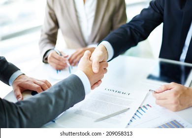 Image Of Business Partners Handshaking Over Business Objects On Workplace