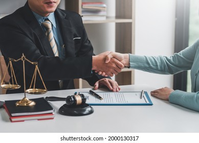 Image of a businessman lawyer shaking hands with a woman client collaboration agreement contract document and a mallet placed at a desk.
