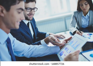 Image of businessman pointing at document in touchpad while interacting with his partner at meeting
