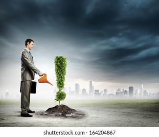 Image of businessman watering plant shaped like exclamation mark
