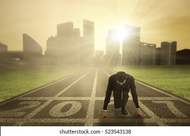 Image of businessman wearing a formal suit in ready position to chase his success with numbers 2017 on the asphalt track 