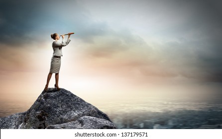 Image of businesswoman looking in telescope standing atop of rock