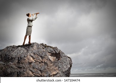 Image of businesswoman looking in telescope standing atop of rock