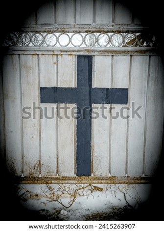 The image captures a black cross at the entrance of the cemetery gate. Symbolizing serenity and commemoration, the cross stands solemn, bringing an atmosphere of reflection to this sacred place.