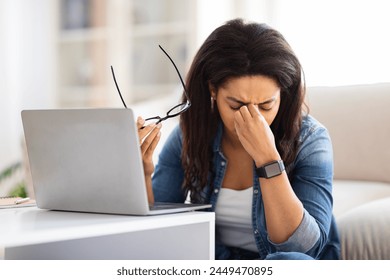 The image captures a black lady at home evidently stressed or overwhelmed, holding her glasses away from a laptop, illustrating common work-from-home challenges - Powered by Shutterstock