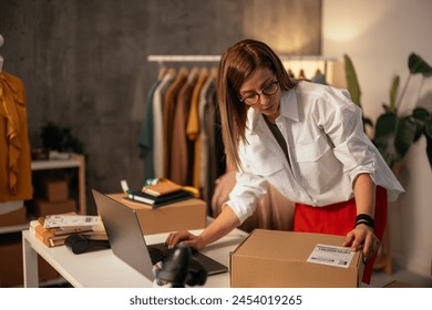 The image captures a businesswoman earnestly scanning a package barcode with her computer and phone nearby, in a fashion warehouse - Powered by Shutterstock