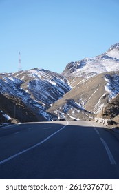 The image captures a close-up view of a rugged, snow-capped mountain peak in the Atlas Mountains. The rocky terrain is sharply defined, with patches of snow clinging to the higher elevations.