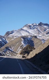 The image captures a close-up view of a rugged, snow-capped mountain peak in the Atlas Mountains. The rocky terrain is sharply defined, with patches of snow clinging to the higher elevations.