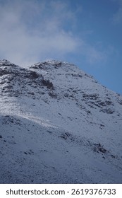 The image captures a close-up view of a rugged, snow-capped mountain peak in the Atlas Mountains. The rocky terrain is sharply defined, with patches of snow clinging to the higher elevations.