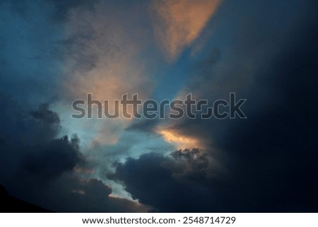 The image captures a dramatic and contrasting moment in the sky. Dark, dense clouds, heavy with rain, dominate most of the scene, creating a gloomy and stormy atmosphere. However, a beam of light filt