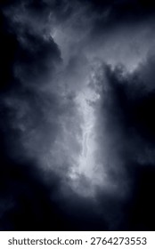 The image captures a dramatic expanse of dark, turbulent storm clouds filling the entire frame. There is no visible horizon, land, or human-made structure—only the sky, heavy and brooding, as if on the verge of unleashing rain or thunder. The clouds vary in density and tone, ranging from deep charcoal and navy hues to lighter grays that glow faintly where light filters through.At the top of the image, the clouds are especially dense and dark, forming a thick canopy that feels weighty and oppressive. A lighter band of cloud stretches horizontally across the middle of the frame, acting as a visual break between the darker masses above and below.