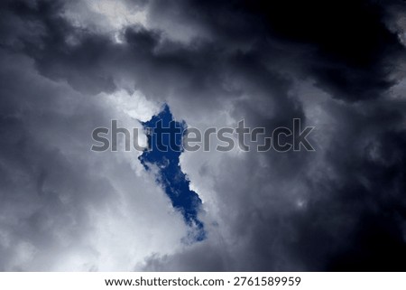 The image captures a dramatic expanse of dark, turbulent storm clouds filling the entire frame. There is no visible horizon, land, or human-made structure—only the sky, heavy and brooding, as if on the verge of unleashing rain or thunder. The clouds vary in density and tone, ranging from deep charcoal and navy hues to lighter grays that glow faintly where light filters through.At the top of the image, the clouds are especially dense and dark, forming a thick canopy that feels weighty and oppressive. A lighter band of cloud stretches horizontally across the middle of the frame, acting as a visual break between the darker masses above and below.