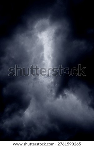 The image captures a dramatic expanse of dark, turbulent storm clouds filling the entire frame. There is no visible horizon, land, or human-made structure—only the sky, heavy and brooding, as if on the verge of unleashing rain or thunder. The clouds vary in density and tone, ranging from deep charcoal and navy hues to lighter grays that glow faintly where light filters through.At the top of the image, the clouds are especially dense and dark, forming a thick canopy that feels weighty and oppressive. A lighter band of cloud stretches horizontally across the middle of the frame, acting as a visual break between the darker masses above and below.