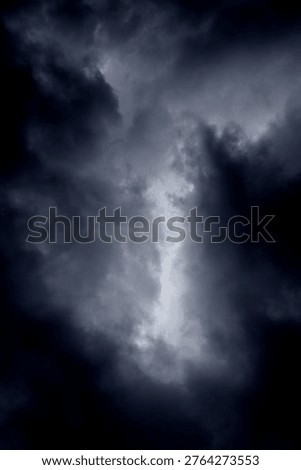 The image captures a dramatic expanse of dark, turbulent storm clouds filling the entire frame. There is no visible horizon, land, or human-made structure—only the sky, heavy and brooding, as if on the verge of unleashing rain or thunder. The clouds vary in density and tone, ranging from deep charcoal and navy hues to lighter grays that glow faintly where light filters through.At the top of the image, the clouds are especially dense and dark, forming a thick canopy that feels weighty and oppressive. A lighter band of cloud stretches horizontally across the middle of the frame, acting as a visual break between the darker masses above and below.