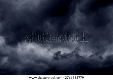 The image captures a dramatic expanse of dark, turbulent storm clouds filling the entire frame. There is no visible horizon, land, or human-made structure—only the sky, heavy and brooding, as if on the verge of unleashing rain or thunder. The clouds vary in density and tone, ranging from deep charcoal and navy hues to lighter grays that glow faintly where light filters through.At the top of the image, the clouds are especially dense and dark, forming a thick canopy that feels weighty and oppressive. A lighter band of cloud stretches horizontally across the middle of the frame, acting as a visual break between the darker masses above and below.