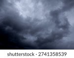 The image captures a dramatic expanse of sky dominated by towering storm clouds. Thick, heavy masses of dark gray and charcoal clouds loom from both sides of the frame, curving inward as if closing around a brighter opening at the center. The clouds appear dense and textured, with soft, billowing edges that suggest constant movement and turbulence. Their forms are layered and sculpted, with deeper shadows pooling in the folds and lighter grays tracing the contours where faint light filters through.
At the center of the composition, a pale, diffused glow breaks through the gloom. This lighter patch of sky, almost silvery in tone, creates a striking contrast against the surrounding darkness. It feels like a temporary clearing, a narrow corridor of light between two advancing walls of cloud. The brightness does not come from direct sunlight but rather from sunlight obscured by thick vapor, giving the scene a moody, atmospheric quality.
The left side of the image shows clouds with slightly more variation in tone, where subtle gradations of gray transition from smoky light to near-black. The right side appears heavier and darker, with a more imposing, shadowed presence. The cloud formations rise upward and inward, giving the impression of height and scale, as though the viewer is looking up from the ground at a vast, shifting ceiling of weather.
There are no visible landmarks, buildings, or horizon lines—only sky. This absence of grounding elements enhances the feeling of immersion, as if the viewer is enveloped by the storm. The image conveys tension and anticipation, suggesting that rain or thunder may soon follow. At the same time, the central glow hints at resilience and contrast—light pushing gently against encroaching darkness. The overall mood is powerful, contemplative, and slightly ominous, capturing the raw, ever-changing drama of the atmosphere.