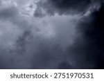 The image captures a dramatic expanse of sky dominated by towering storm clouds. Thick, heavy masses of dark gray and charcoal clouds loom from both sides of the frame, curving inward as if closing around a brighter opening at the center. The clouds appear dense and textured, with soft, billowing edges that suggest constant movement and turbulence. Their forms are layered and sculpted, with deeper shadows pooling in the folds and lighter grays tracing the contours where faint light filters through.
At the center of the composition, a pale, diffused glow breaks through the gloom. This lighter patch of sky, almost silvery in tone, creates a striking contrast against the surrounding darkness. It feels like a temporary clearing, a narrow corridor of light between two advancing walls of cloud. The brightness does not come from direct sunlight but rather from sunlight obscured by thick vapor, giving the scene a moody, atmospheric quality.
The left side of the image shows clouds with slightly more variation in tone, where subtle gradations of gray transition from smoky light to near-black. The right side appears heavier and darker, with a more imposing, shadowed presence. The cloud formations rise upward and inward, giving the impression of height and scale, as though the viewer is looking up from the ground at a vast, shifting ceiling of weather.
There are no visible landmarks, buildings, or horizon lines—only sky. This absence of grounding elements enhances the feeling of immersion, as if the viewer is enveloped by the storm. The image conveys tension and anticipation, suggesting that rain or thunder may soon follow. At the same time, the central glow hints at resilience and contrast—light pushing gently against encroaching darkness. The overall mood is powerful, contemplative, and slightly ominous, capturing the raw, ever-changing drama of the atmosphere.