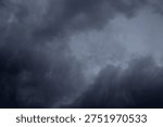 The image captures a dramatic expanse of sky dominated by towering storm clouds. Thick, heavy masses of dark gray and charcoal clouds loom from both sides of the frame, curving inward as if closing around a brighter opening at the center. The clouds appear dense and textured, with soft, billowing edges that suggest constant movement and turbulence. Their forms are layered and sculpted, with deeper shadows pooling in the folds and lighter grays tracing the contours where faint light filters through.
At the center of the composition, a pale, diffused glow breaks through the gloom. This lighter patch of sky, almost silvery in tone, creates a striking contrast against the surrounding darkness. It feels like a temporary clearing, a narrow corridor of light between two advancing walls of cloud. The brightness does not come from direct sunlight but rather from sunlight obscured by thick vapor, giving the scene a moody, atmospheric quality.
The left side of the image shows clouds with slightly more variation in tone, where subtle gradations of gray transition from smoky light to near-black. The right side appears heavier and darker, with a more imposing, shadowed presence. The cloud formations rise upward and inward, giving the impression of height and scale, as though the viewer is looking up from the ground at a vast, shifting ceiling of weather.
There are no visible landmarks, buildings, or horizon lines—only sky. This absence of grounding elements enhances the feeling of immersion, as if the viewer is enveloped by the storm. The image conveys tension and anticipation, suggesting that rain or thunder may soon follow. At the same time, the central glow hints at resilience and contrast—light pushing gently against encroaching darkness. The overall mood is powerful, contemplative, and slightly ominous, capturing the raw, ever-changing drama of the atmosphere.