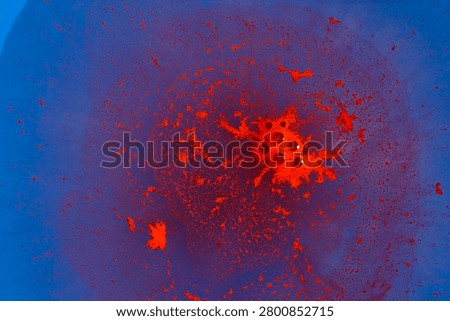 The image captures a dramatic splatter of red paint over a blue backdrop